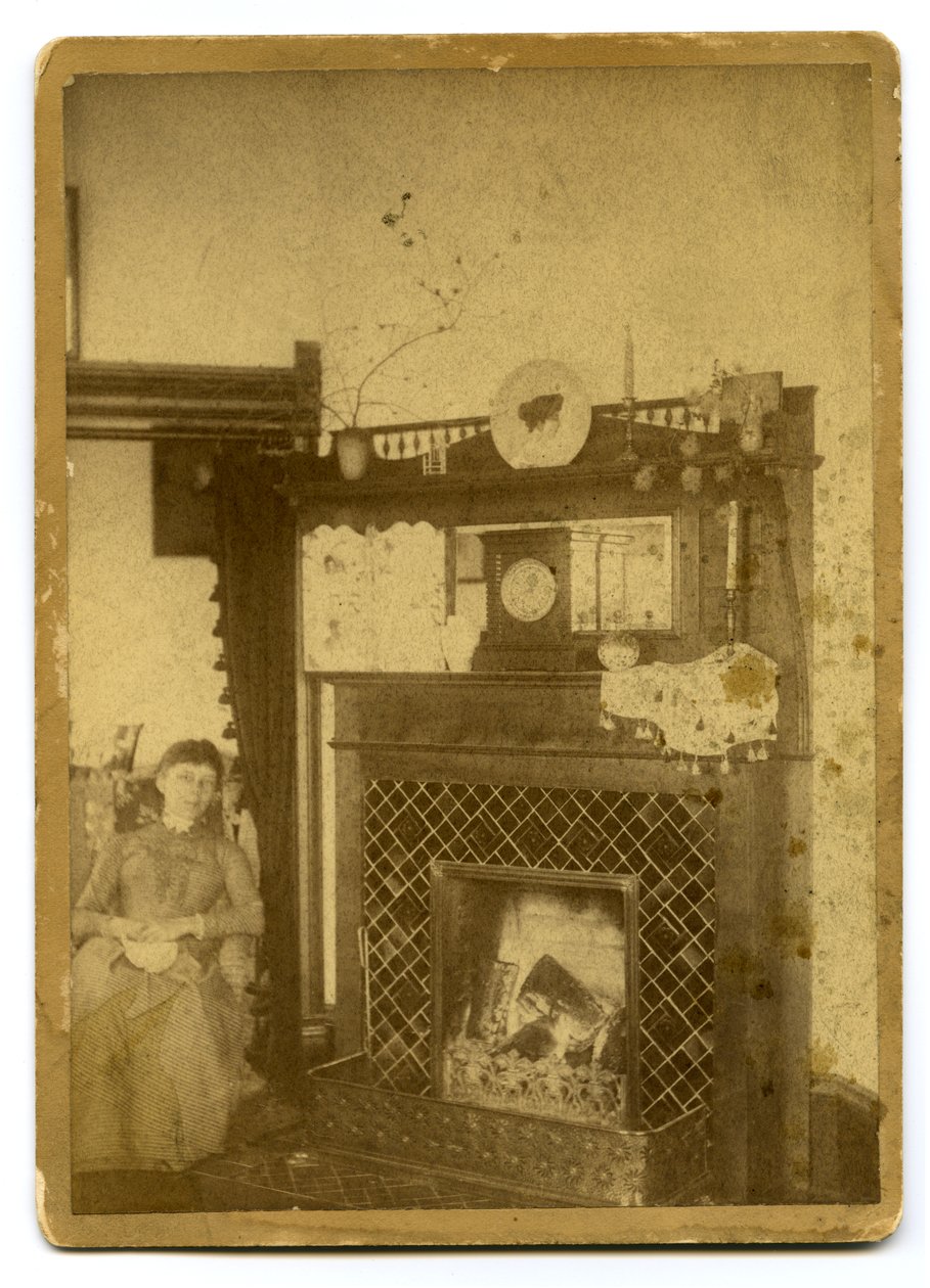 Frau sitzt neben einem brennenden Kamin von Unknown