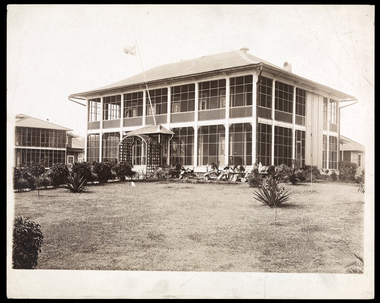 Ein zweistöckiges Haus mit Veranden, mit einer amerikanischen Flagge; in Panama während des Baus des Kanals, 1912 von Byron Company