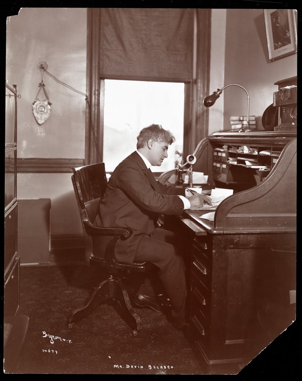 David Belasco schreibt an einem Schreibtisch in den Büros seines Theaters, 1902 von Byron Company