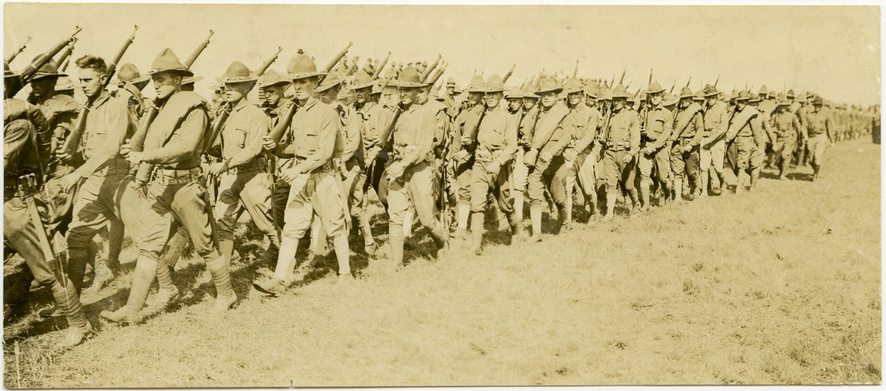 Horizontales, sepiafarbenes Foto, das Reihen uniformierter Soldaten zeigt, die in Formation durch ein Grasfeld marschieren und Gewehre tragen von Carl Michel