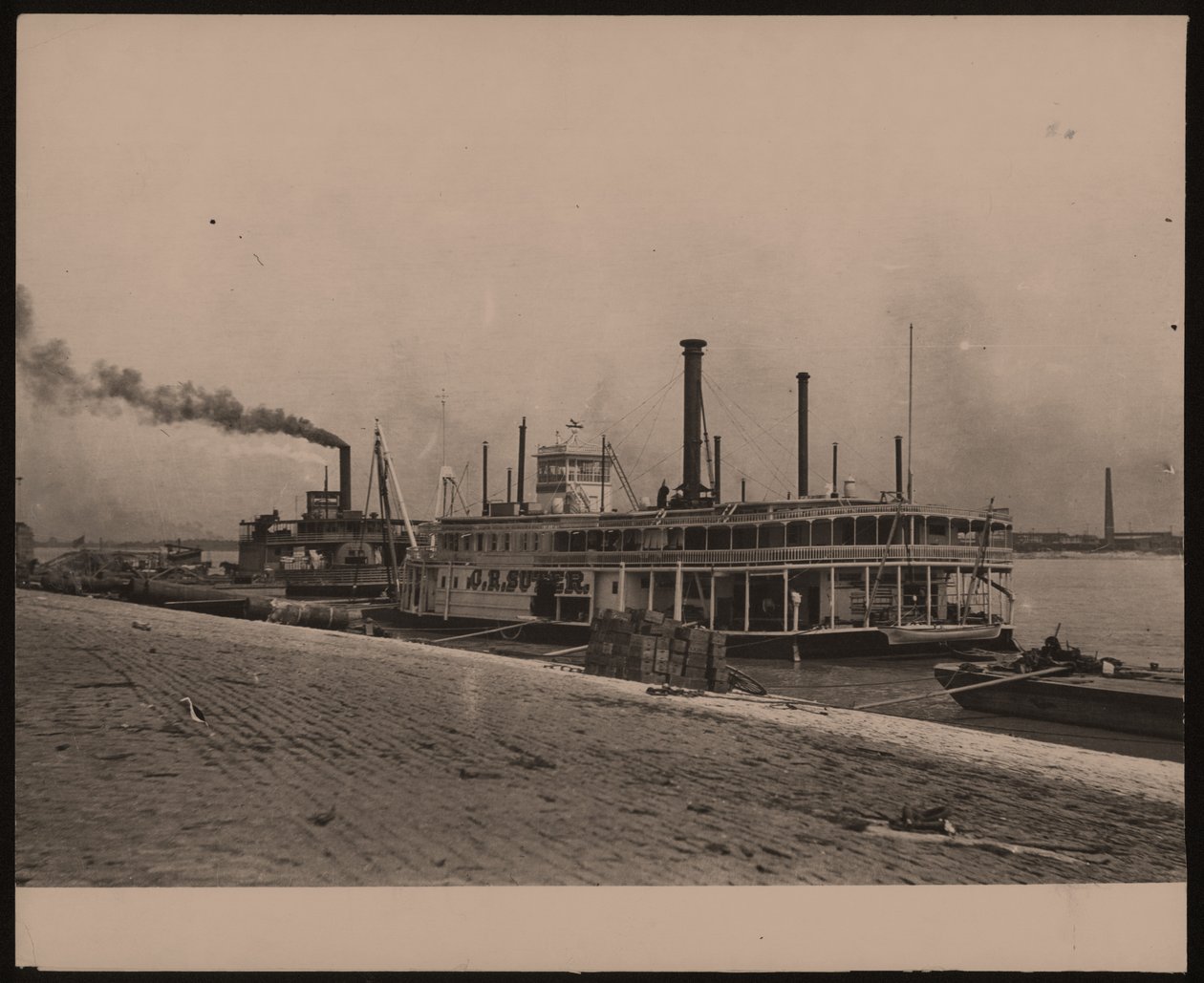 Horizontales Schwarz-Weiß-Foto des Dampfschiffs C.R. Suter. Ein weiteres Dampfschiff ist dahinter geparkt und Kisten sind am Ufer gestapelt von William G. Swekosky